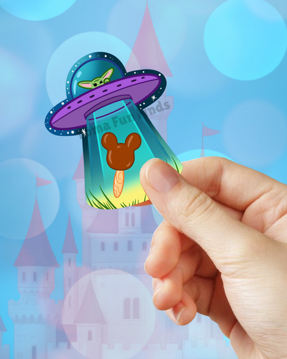 Hand holding a transparent card with a Mickey Mouse head design, UFO, and castle in the background.