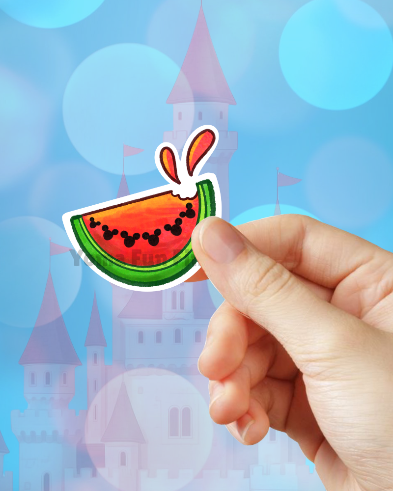 Hand holding a watermelon-shaped sticker with cartoon characters against a castle and blue sky background