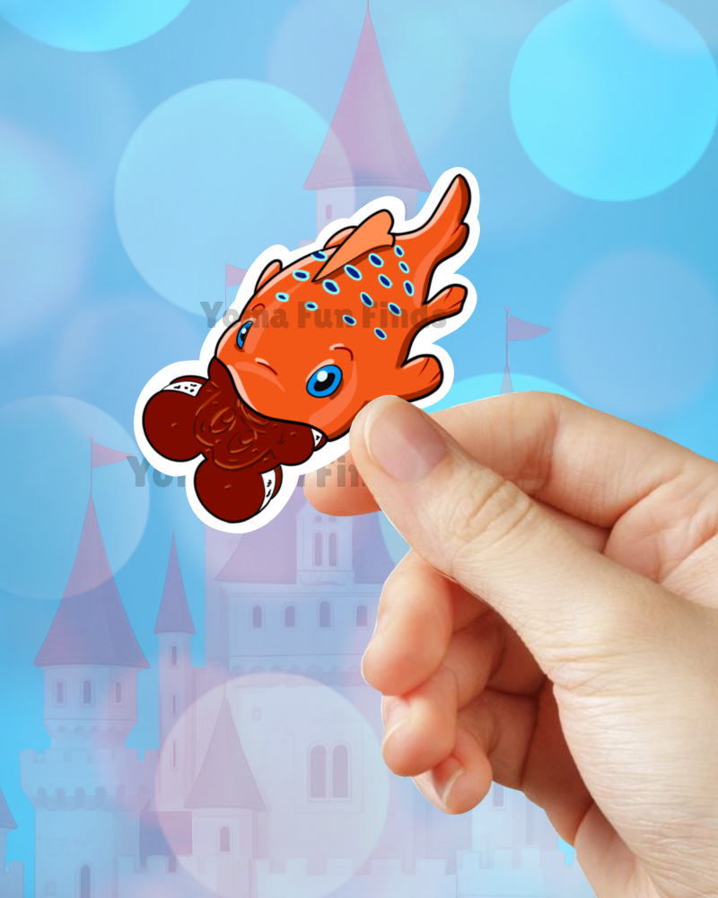 Hand holding a cartoonish orange and brown creature sticker with a castle and blue sky background.
