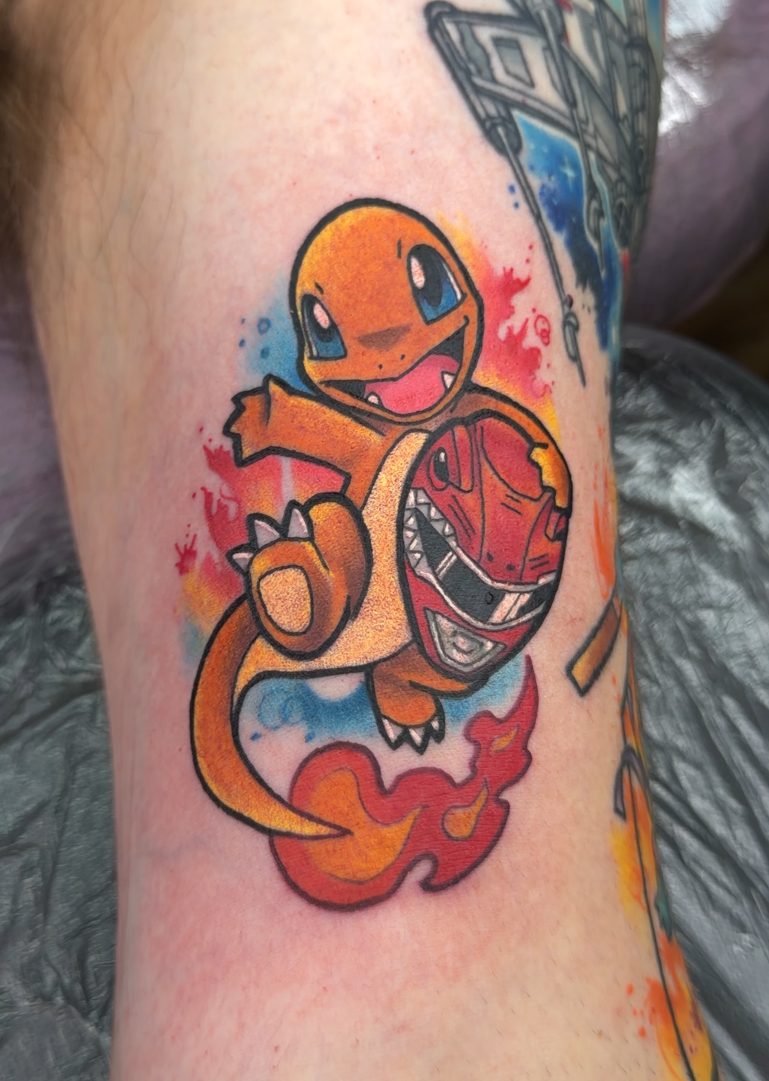 A colorful tattoo of Charmander and its mother on a person's forearm, with other tattoo designs partially visible in the background.