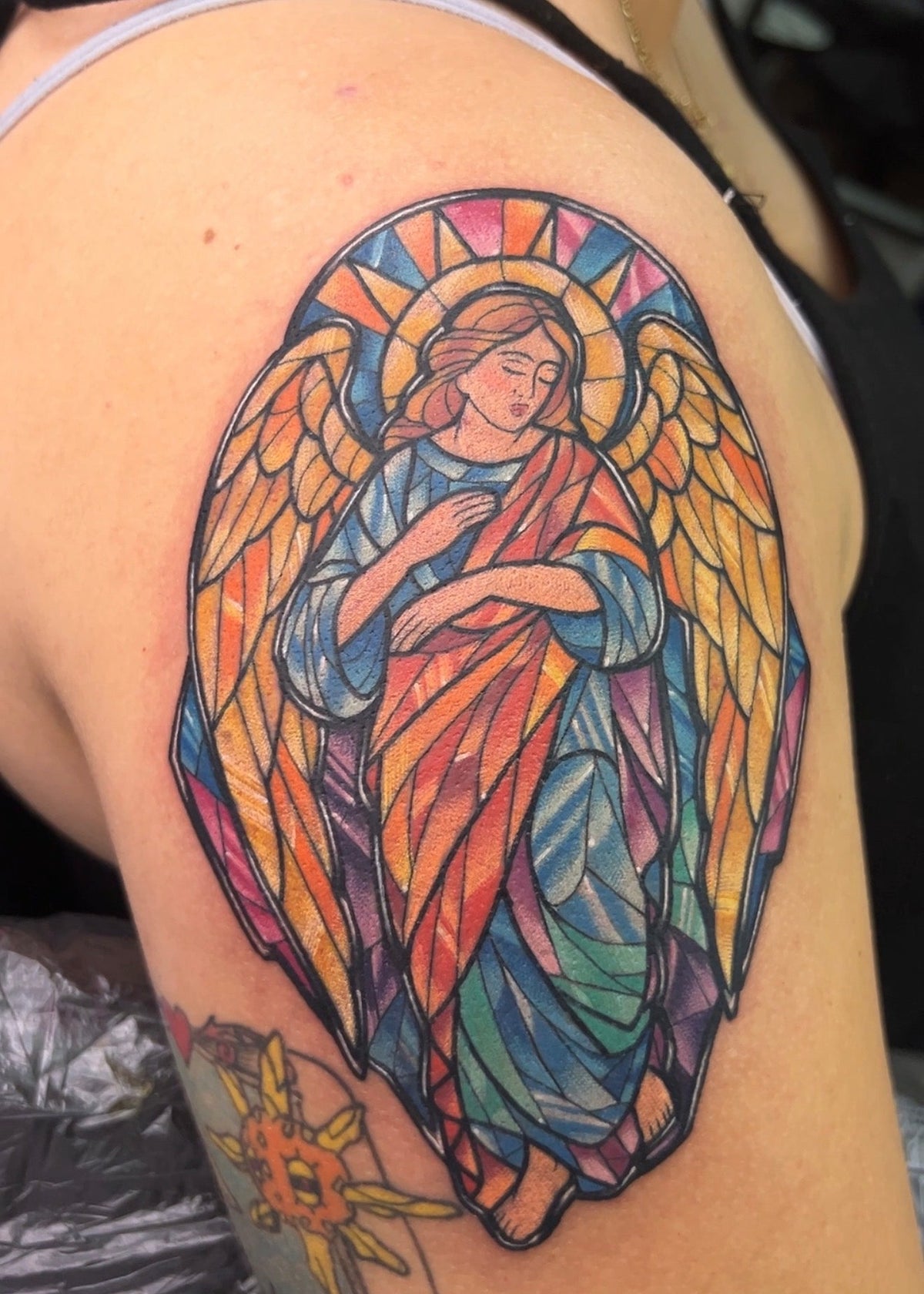 A colorful tattoo of a winged angel in a stained-glass style, shown on a person's upper shoulder.