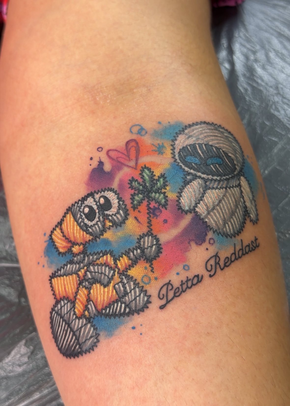 A colorful custom tattoo on a person's forearm, featuring a patchwork-style astronaut, a clownfish, a palm tree, and the text 'Diana Redda' in script.